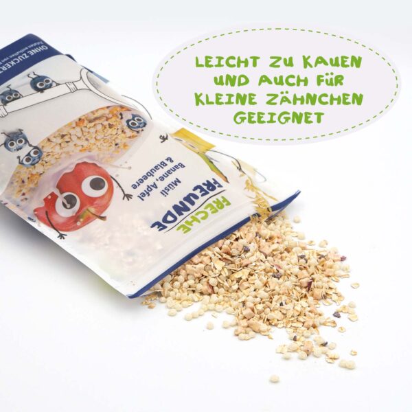 Die geöffnete Packung Freche Freunde Bio Müsli Banane, Apfel & Blaubeere liegt auf der Seite – das Müsli ist teilweise ausgeschüttet. Die frechen Freunde Bibi, Bob und Alfred sind auf der Verpackung abgebildet. Text: „Leicht zu kauen und auch für kleine Zähnchen geeignet“.
