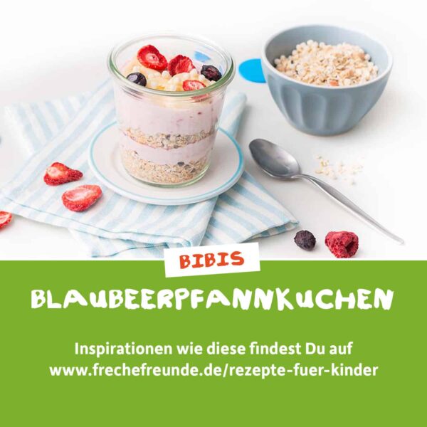 Rezept: Ein geschichtetes Frühstück im Glas mit Müsli, Joghurt und gefriergetrockneten Beeren – daneben ein Löffel und eine Schale mit Müsli. Text: „Bibis Blaubeerpfannkuchen – Inspirationen wie diese findest du auf www.frechefreunde.de/rezepte-fuer-kinder“.