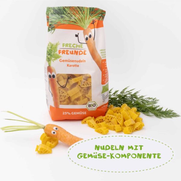Freche Freunde Bio Gemüsenudeln Karotte im 300g-Beutel mit 25 % Gemüseanteil. Neben der geöffneten Verpackung liegt eine Karotte mit Wackelaugen. Text: Nudeln mit Gemüse-Komponente.
