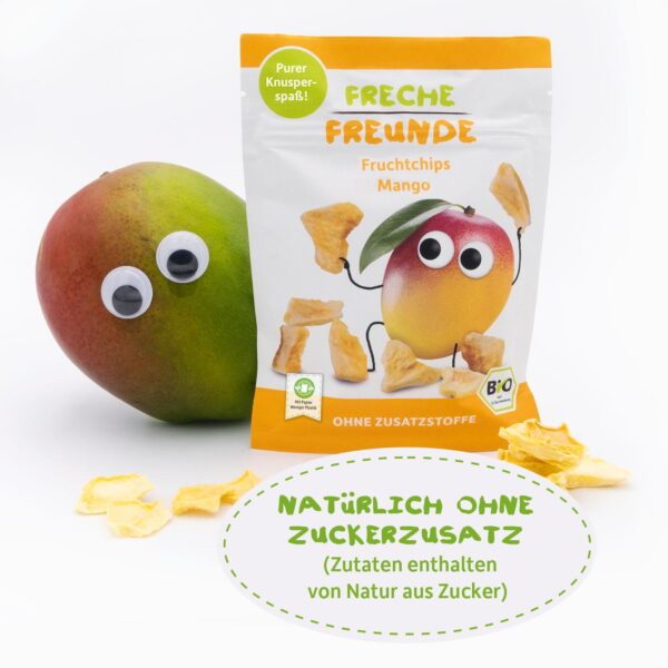 Freche Freunde Bio Fruchtchips Mango mit Momo Mango, der frech hinter der Produktverpackung hervorschaut. Vor dem Beutel liegen knusprige Mangostückchen – ganz ohne Zuckerzusatz. Auf dem Bild steht: „Natürlich ohne Zuckerzusatz (Zutaten enthalten von Natur aus Zucker)“.