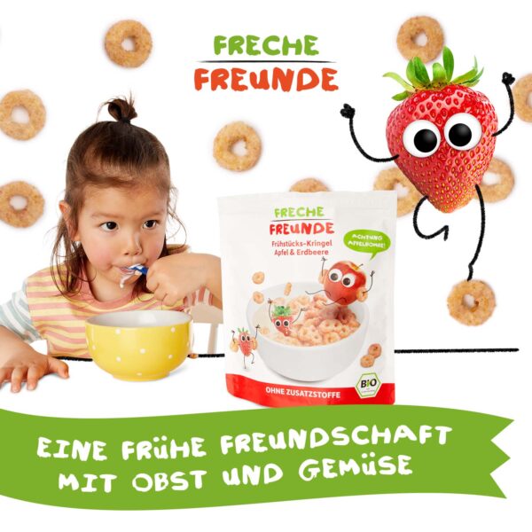 Ein kleines Kind löffelt mit Genuss aus einer gelben Schüssel. Im Vordergrund die Packung Freche Freunde Bio Frühstücks-Kringel Apfel & Erdbeere. Im Hintergrund hüpft Edda Erdbeere mit Kulleraugen frech durchs Bild. Der Slogan: „Eine frühe Freundschaft mit Obst und Gemüse“.