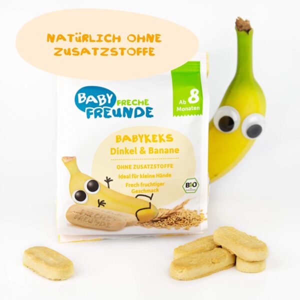 Bobby Banane steht neben der Verpackung der Freche Freunde Bio Babykekse Dinkel & Banane. Die Kekse liegen im Vordergrund