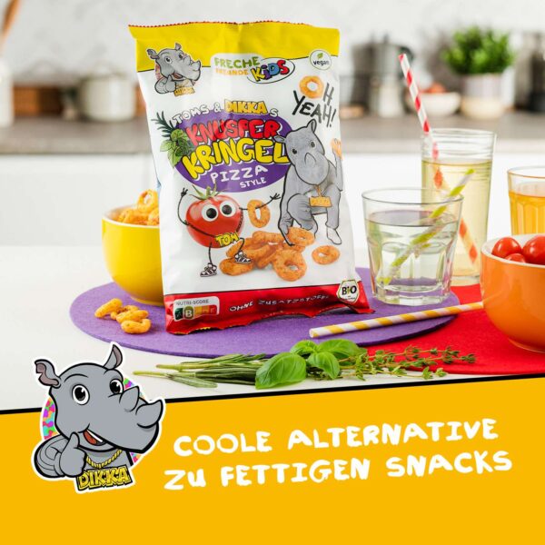 Freche Freunde Kids Bio Knusper Kringel Pizza Style in gemütlicher Küchenkulisse. Die Packung mit Tom Tomate und Dikka Nashorn steht neben einer Schale mit Kringeln, Getränken und frischen Kräutern. Text: "Coole Alternative zu fettigen Snacks".