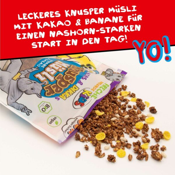 Freche Freunde Bio Bobs & DIKKAs Knusper Müsli Banane & Kakao geöffnet auf weißem Untergrund – der köstliche Mix aus knusprigen Haferstücken, gelben Cornflakes und weißen Crispies ist zu sehen. Aufdruck: „Leckeres Knusper Müsli mit Kakao & Banane für einen Nashorn-starken Start in den Tag!“. Unten das Wort „YO!“