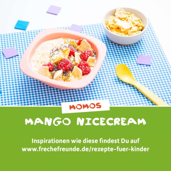 Rezept: Momos Mango-Nicecream mit Himbeeren, Chiasamen und Chips als Topping – serviert in einer rosafarbenen Schüssel auf blau-weißem Picknicktuch. Daneben ein gelber Löffel und weitere Chips in einem weißen Schälchen. Der Text empfiehlt mehr Rezepte auf frechefreunde.de.