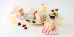 Gemüse-Sandwich mit rosa, grünem & beigem Aufstrich auf einem Teller, daneben Rote Bete Stückchen und aufgeschnittene Avocado