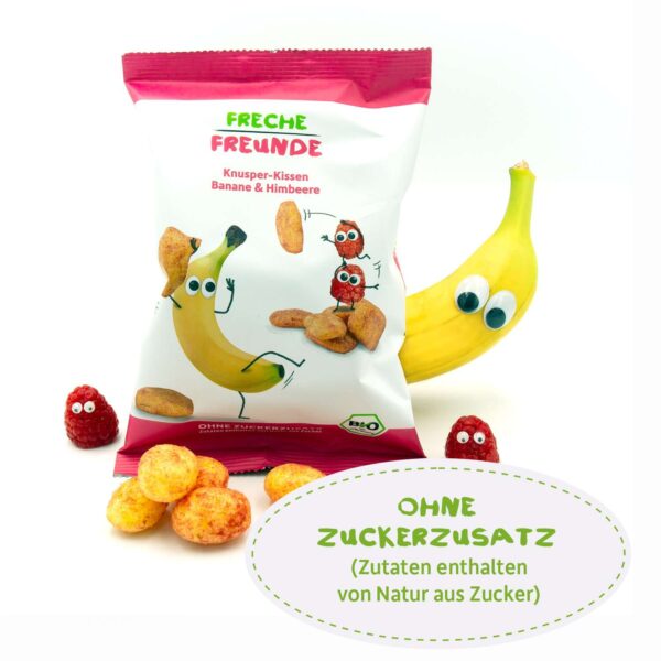 Die Freche Freunde Bio Knusper-Kissen Banane & Himbeere werden von einer echten Banane mit Wackelaugen und Himbeeren begleitet, daneben die Knusper-Kissen. Text: Ohne Zuckerzusatz: Zutaten enthalten von Natur aus Zucker.
