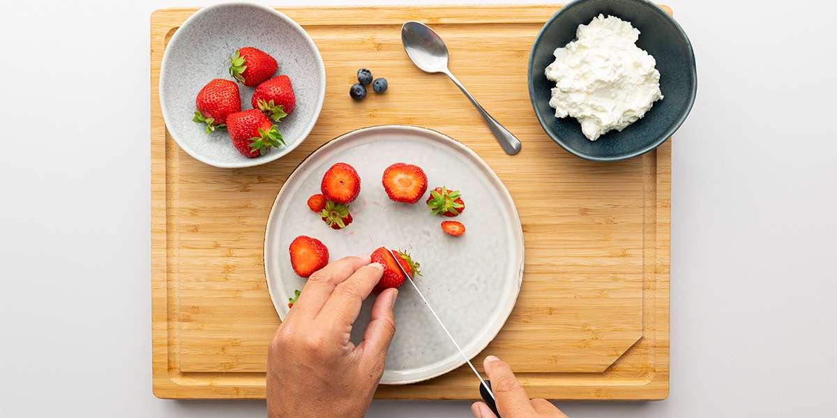 Für die Erdbeer Zwerge werden Erdbeeren mit einem Messer geteilt. Daneben die restlichen Erdbeeren und der Quark.