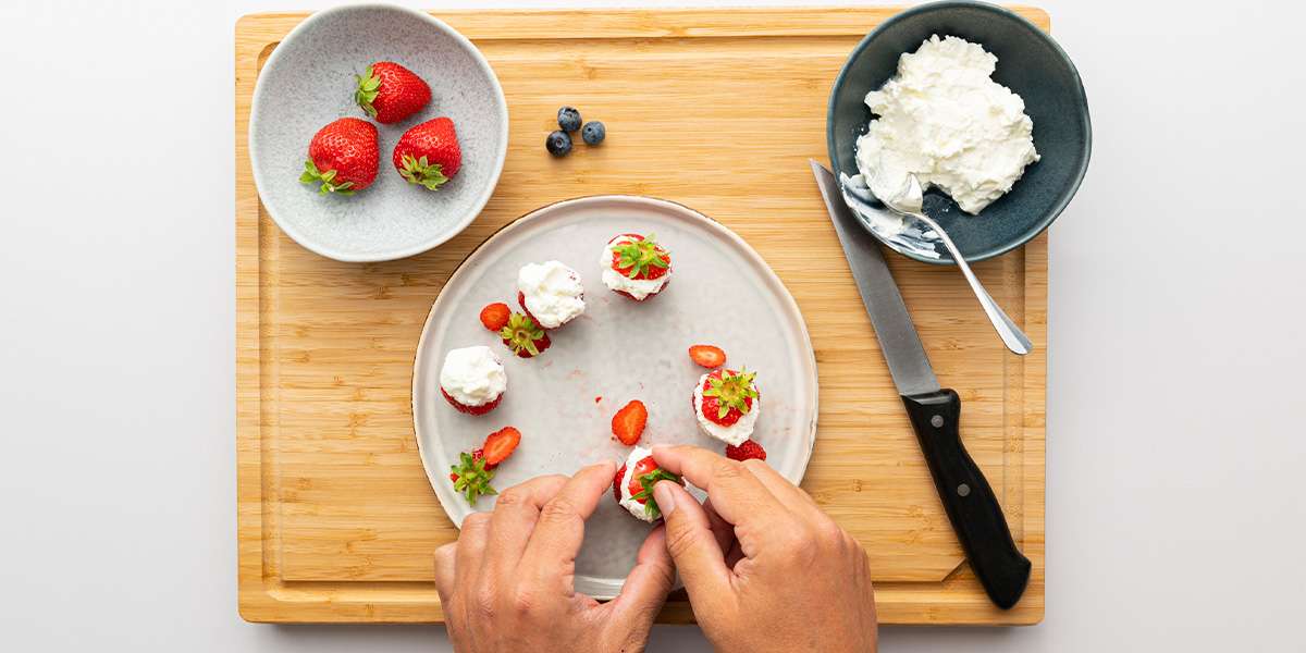 Für die Erdbeer Zwerge wird der Erdbeerteil mit dem Grün zurück auf den Erdbeerteil mit Quark gepackt. Daneben die restlichen Erdbeeren, der Quark und ein Messer.