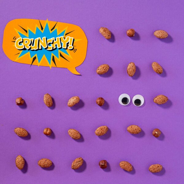 Freche Freunde Kids Bio Crunchy Bits mit einzelnen Crunchy Bits nebeneinander gereiht auf lila Hintergrund, zwischendrin ein paar Wackelaugen und eine Sprechblase wo Crunchy drin steht.