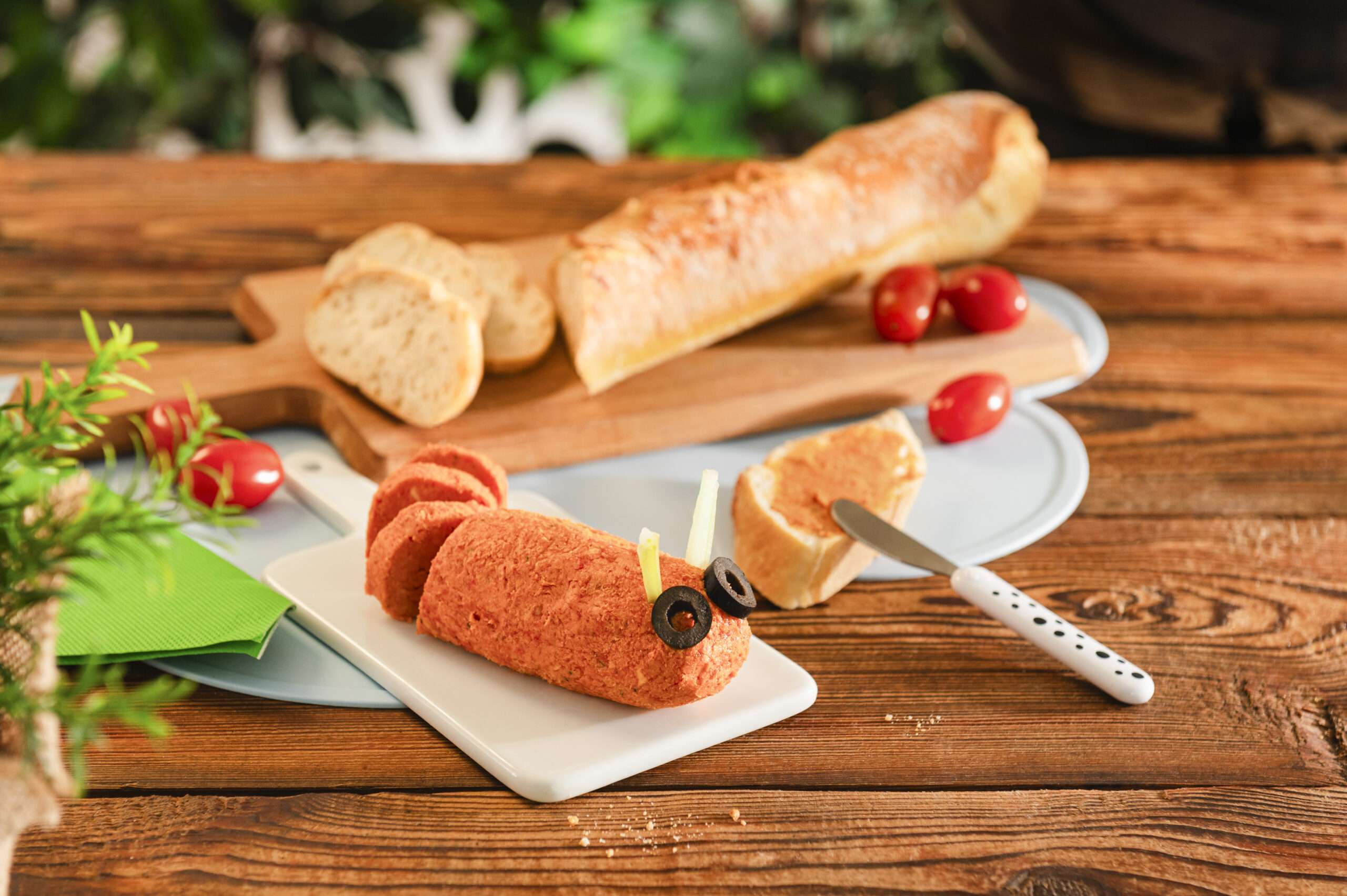 Tomatenbutter auf einem Teller serviert, mit Olivenscheiben als Augen, dazu Baguette
