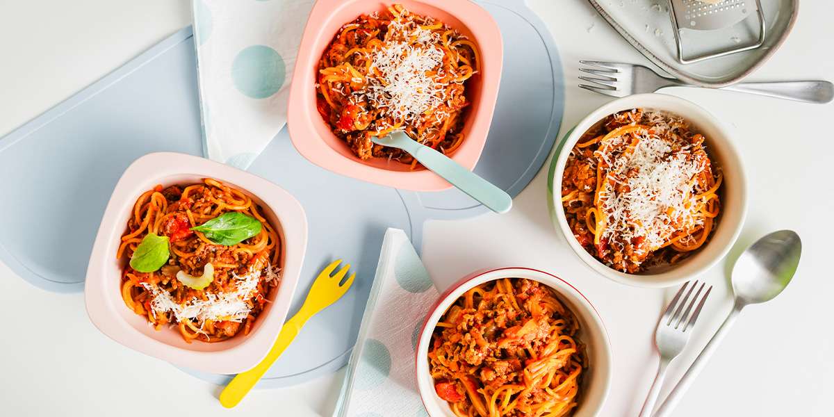 One Pot Spaghetti Bolognese in 4 Tellern angerichtet und mit Parmesan dekoriert. Links und rechts liegen Messer und Gabel sowie Kinderbesteck.