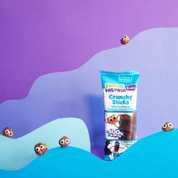Freche Freunde Kids Crunchy Sticks mit Haselnuss, Kakao & Kokos – knusprig verpackt, umgeben von frechen Haselnüssen.