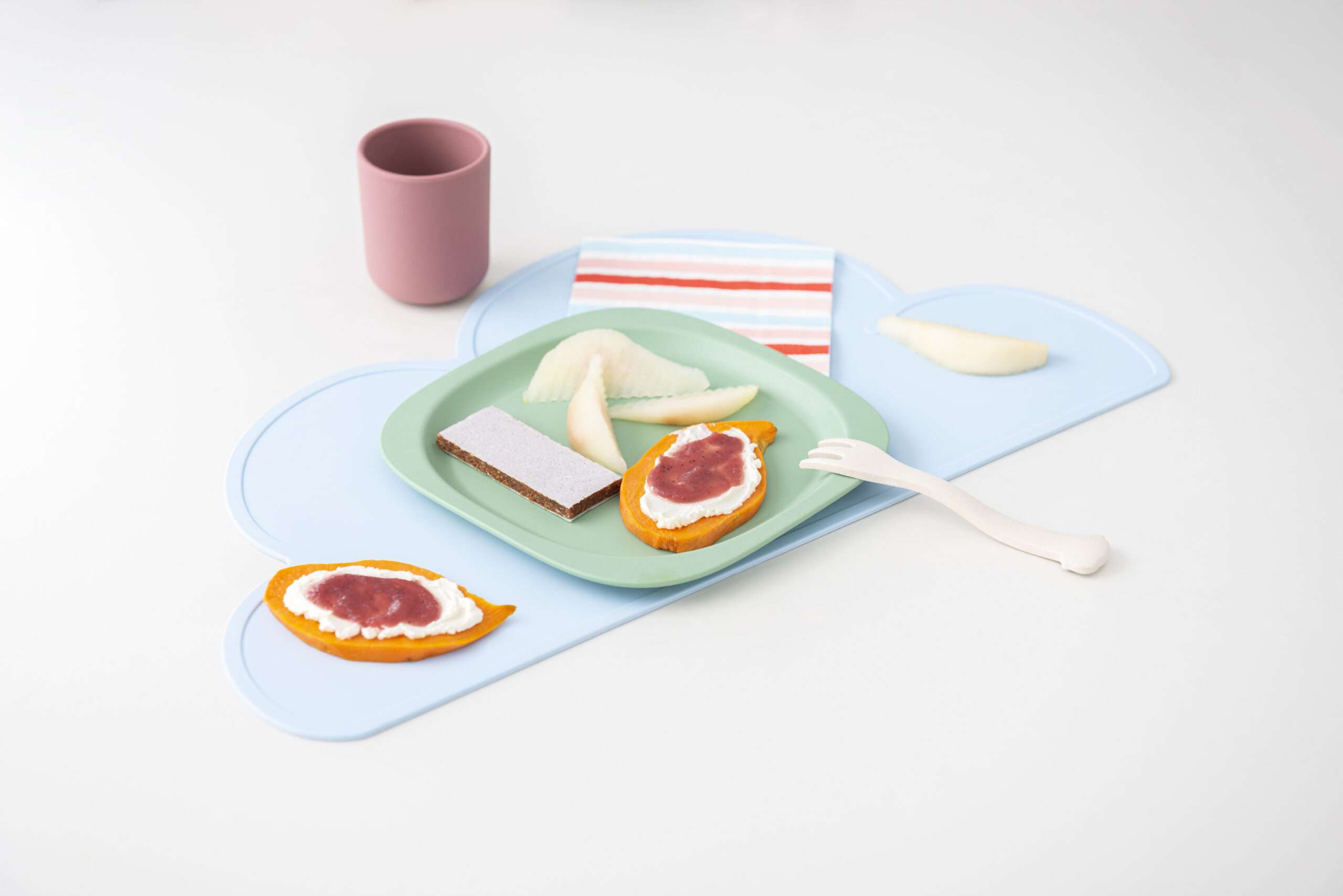 Süßkartoffel-Schnitte mit Frischkäse und Obstbrei, dazu Birnenspalten und Stücke eines Früchte-Riegels auf einem Teller