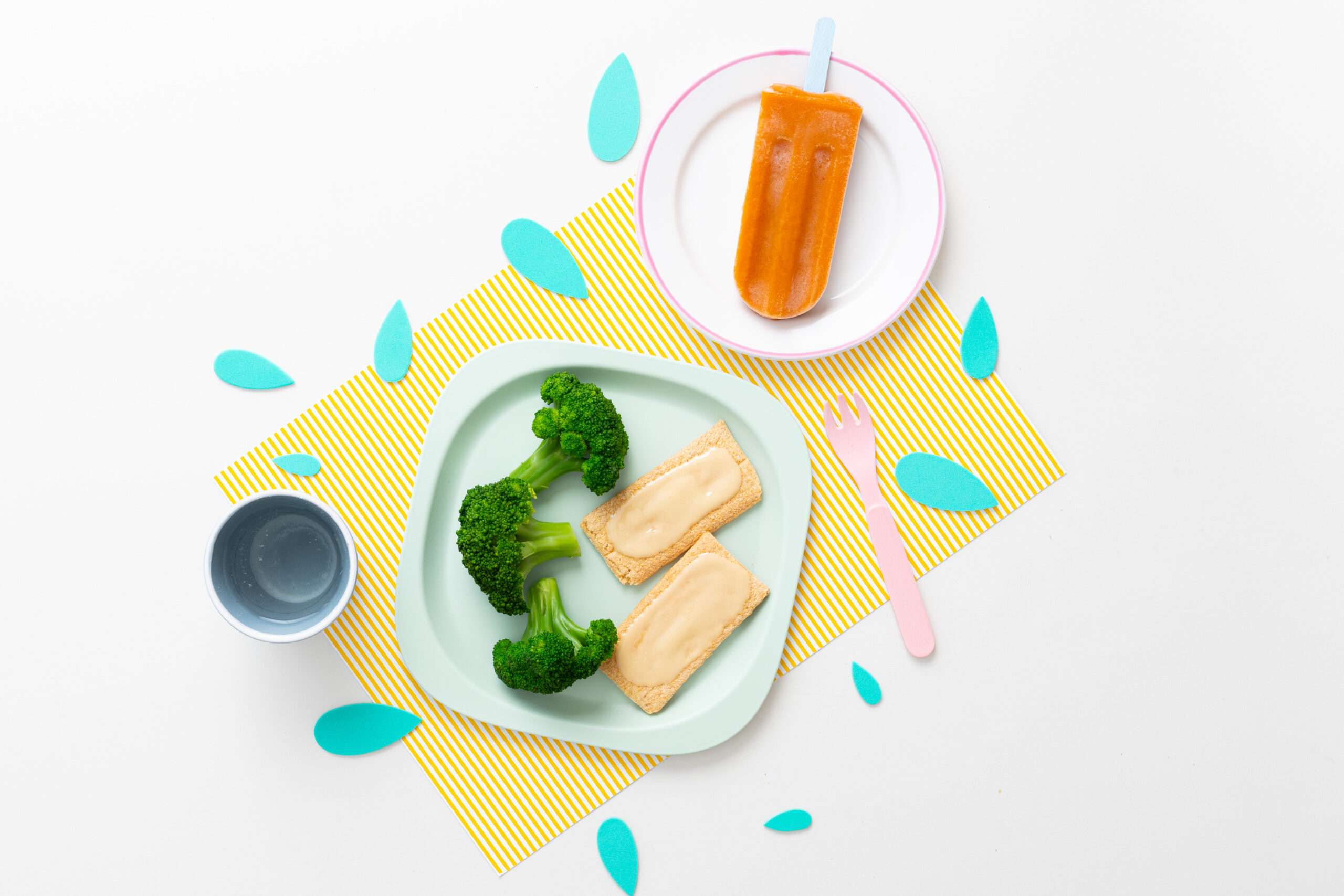 Mango-Eis am Stiel, Knusperschnitten & Brokkoli auf einem Teller serviert dazu ein Becher Wasser