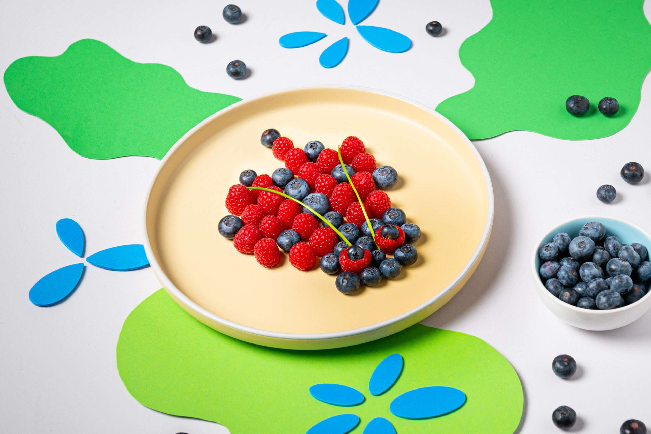 Himbeeren & Blaubeeren in Form eines Käfers auf einem Teller angerichtet. 2 Schnittlauchhalme sind die Fühler.