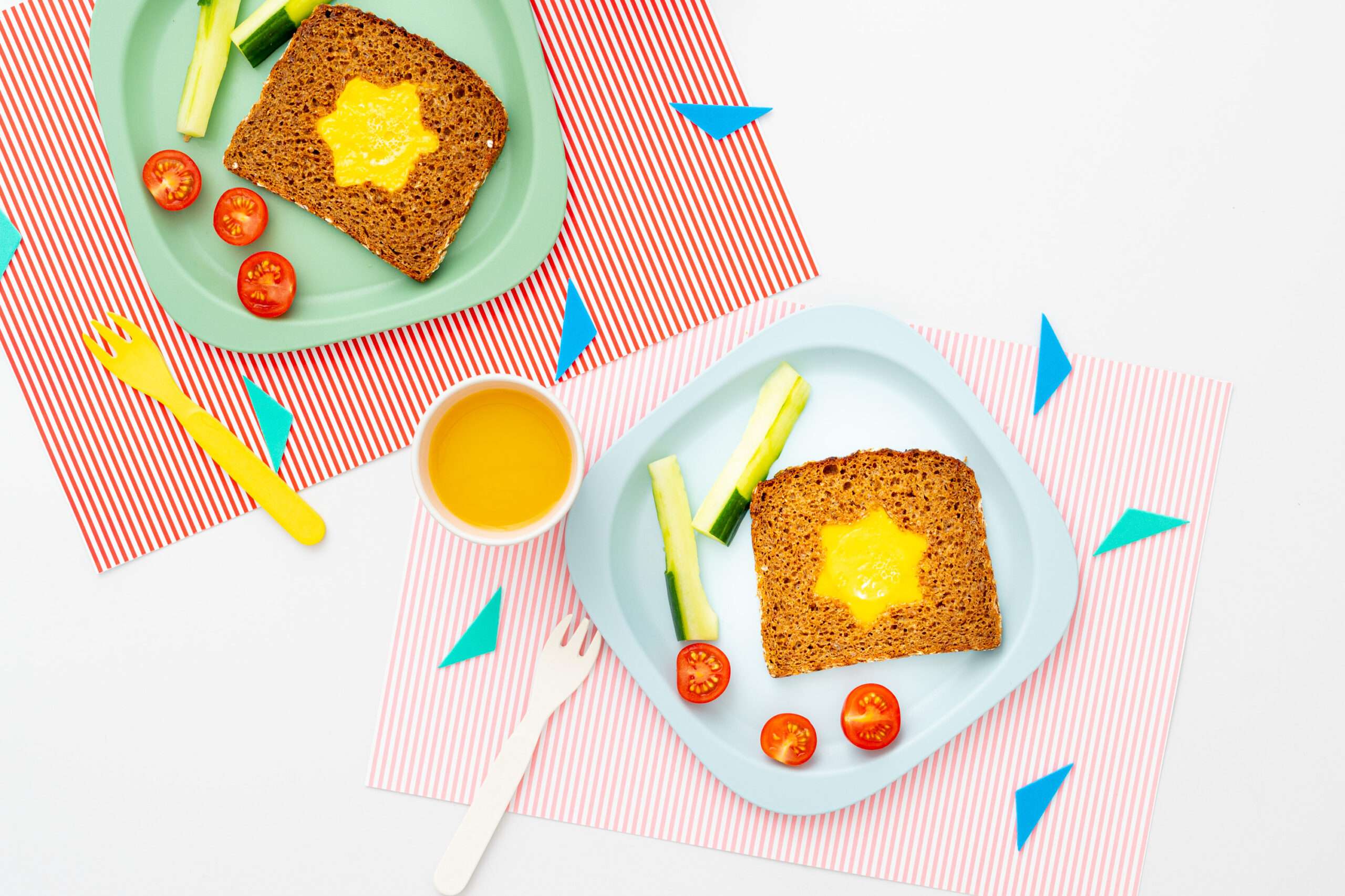 Sternförmies Ei im Brot auf einem Teller serviert mit Gurkensticks & Tomaten dazu ein Becher Orangensaft.