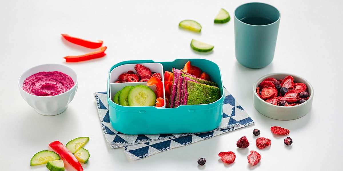 Glutenfreie Pfannkuchen in einer Brotdose zusammen mit frischen Gurkenscheiben, Paprikastreifen und Fruchtchips